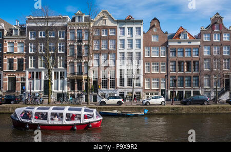 Tall stretto canale case e una gita turistica in barca di crociera sui canali di Amsterdam, in Olanda, in Europa Foto Stock