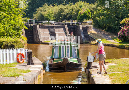 Canal narrowboat che passa attraverso chiuse sul canale Trent e Mersey mentre passa attraverso il villaggio di Wheelock Cheshire Inghilterra Foto Stock