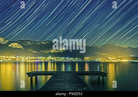 Tracce stellari sul Mont Veyrier, Mont Baron, Mont Baret; si affaccia la riflessione della luce da Veyrier du Lac & Menthon Saint Bernard in Lago di Annecy Foto Stock