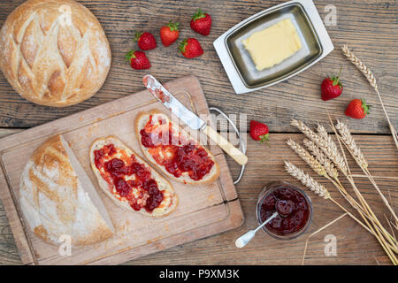 Confettura di fragole su pane di grano e di fragole su uno sfondo di legno Foto Stock