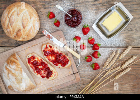 Confettura di fragole su pane di grano e di fragole su uno sfondo di legno Foto Stock