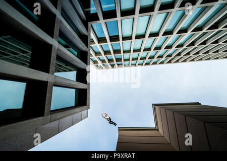 Vista dal basso del maschio atleta di parkour saltando da un tetto a un altro Foto Stock