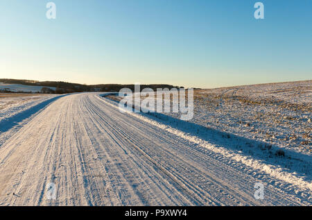 Una strada di campagna ricoperta di neve con le vie e le piste da ruote di automobili, un paesaggio invernale, una svolta a destra, gli alberi crescono all'orizzonte, a l Foto Stock