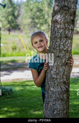 Bella ragazza bionda, con berretto da baseball, che spuntavano da dietro a un albero. Modello di Rilascio #113 Foto Stock