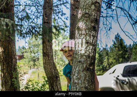 Bella ragazza bionda, con berretto da baseball, che spuntavano da dietro a un albero. Modello di Rilascio #113 Foto Stock