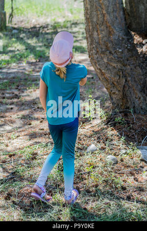 Bella ragazza bionda, in baseball hat e vestito blu, smiljng alla telecamera come si siede nell'ombra di un albero. Modello di Rilascio #113 Foto Stock