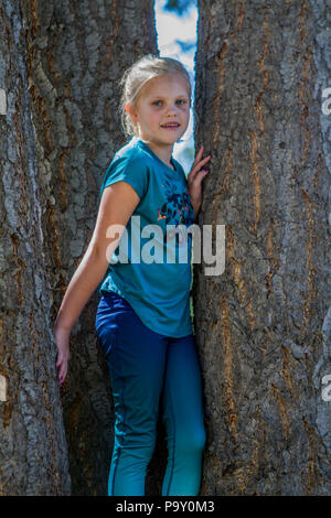 Bella ragazza bionda, in baseball hat e vestito blu, smiljng alla telecamera come si siede nell'ombra di un albero. Modello di Rilascio #113 Foto Stock