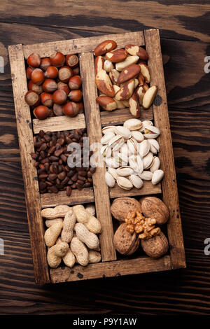 Vari dadi selezione: arachidi, nocciole, castagne, noci, pistacchi e le noci pecan in una scatola di legno. Vista superiore Foto Stock