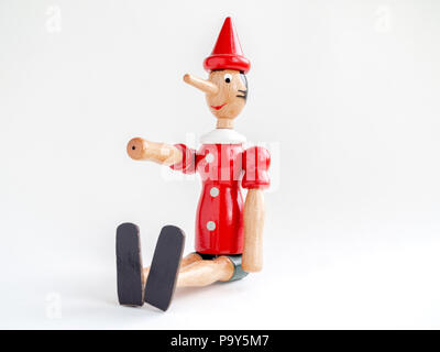 Pinocchio in legno bambola seduta e la mano in alto isolato su sfondo bianco. Foto Stock