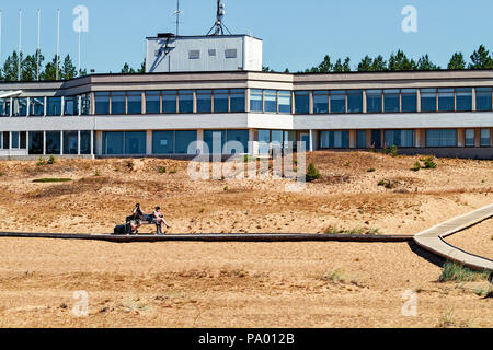 Un giovane seduto su una panchina dalla Boardwalk presso la spiaggia di Kalajoki, Finlandia. Il stile retrò hotel in background sembra essere costruito nel 70s. Foto Stock