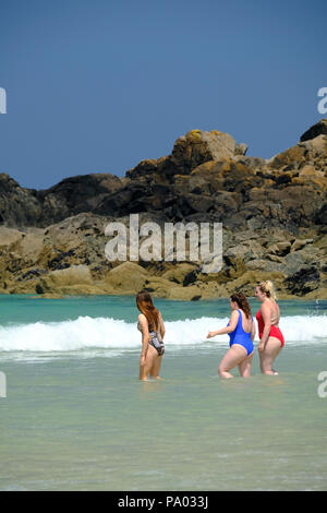 Tre giovani donne in costume da bagno a piedi in mare in una calda giornata estiva su Porthmeor Beach di St Ives in Cornovaglia Foto Stock