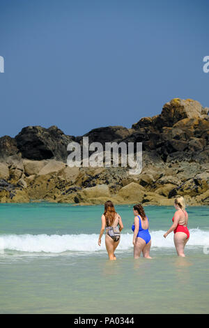 Tre giovani donne in costume da bagno a piedi in mare in una calda giornata estiva su Porthmeor Beach di St Ives in Cornovaglia Foto Stock