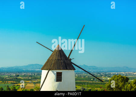 Bellissimo Antico Borgo Medievale bianco mulino a vento nella valle con vegetazione verde alberi prati di montagna e cielo blu sullo sfondo. Splendido panorama del paesaggio Foto Stock