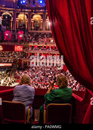 ALBERT HALL INTERNO BBC Proms prestazioni con colleghe in primo piano la visione di musica le prestazioni utilizzando occhiali opera insediato nel lusso in velluto rosso casella privato con platea e palco orchestra palco in background Foto Stock