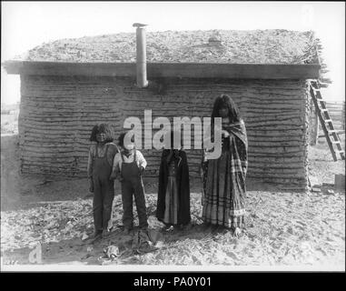 . Inglese: Quattro Mojave bambini indiani in piedi di fronte ad una piccola abitazione con il tetto di paglia, vicino a Yuma, ca.1900 Fotografia di 4 Mojave bambini indiani in piedi di fronte ad una piccola abitazione con il tetto di paglia, vicino a Yuma, ca.1900. Il 2 ragazzi piccoli sono indossando tute da lavoro, il 2 bambine sono entrambi indossando coperte o grandi scialli che raggiunge la terra sulle loro spalle e abiti lunghi. Un tubo di stufa bastoni fuori della parete della dimora dietro di loro. Una scaletta è visibile dietro la casa a destra. Chiamare il numero: CHS-1278 Fotografo: Pierce, C.C. (Charles C.), 1861-1946 Filename: Foto Stock