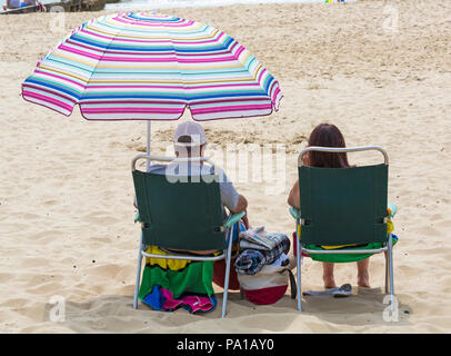 Bournemouth Dorset, Regno Unito. Il 20 luglio 2018. Regno Unito: clima caldo e umido con sole nebuloso a Bournemouth, come sunseekers in testa al mare a Bournemouth spiagge per godersi il bel tempo. Giovane seduto in sedie sotto ombrellone colorato. Credito: Carolyn Jenkins/Alamy Live News Foto Stock