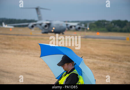 Farnborough, Hampshire, Regno Unito. 20 Luglio, 2018. Giornata conclusiva della biennale Farnborough Commercio Internazionale FIA Airshow2018, tipicamente un giorno di transizione come i clienti business lasciare in getti di VIP e i membri del pubblico arriva a guardare il build-up per il weekend airshow di pubblico. Una guardia di sicurezza è ignaro della grande Boeing C-17 Globemaster III i velivoli militari da trasporto della US Air Force parcheggio dietro di lui. Credito: Malcolm Park/Alamy Live News. Foto Stock