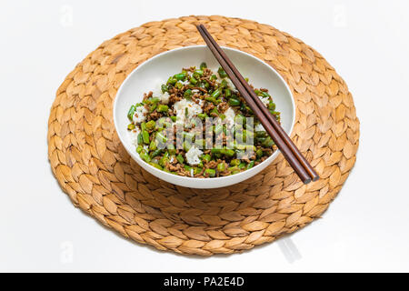 Ciotola di carne bovina macinata spezzatino con fagioli rotonda servita con riso bollito con bacchette su un round stuoia di paglia Foto Stock