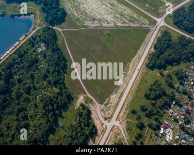 Fotografare da un quadrocopter ad un grande villaggio con piccole case, una foresta verde e un grande campo in una calda e soleggiata giornata estiva Foto Stock