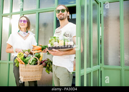 Giovane coppia vegetariana andando fuori mercato sacco di contenimento e una scatola piena di appena acquistato prodotti freschi Foto Stock