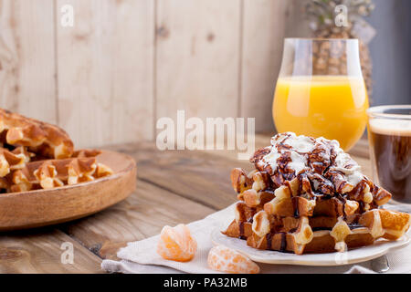 Dolce cialde belghe per colazione, decorata con crema bianca e salsa al cioccolato. Vetro con caffè nero e succo d'arancia, frutta banane e grapfruit. Spazio libero per il testo o per la pubblicità. Foto Stock
