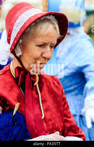 Bionda donna senior, 60s, close up ritratto. Indossando il cofano e matching dress, costume Vittoriano, parte di Dickens settimana l'evento. Candid shot. Foto Stock