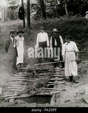 . Inglese: Titolo: cinque uomini spitted cottura carne sul barbecue pit in ambiente rurale. inizio novecento 654 cinque uomini spitted cottura carne sul barbecue pit in ambiente rurale Foto Stock