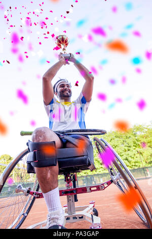 I giovani disabili giocatore di tennis alza la coppa al cielo dopo aver vinto il torneo per esterni Foto Stock