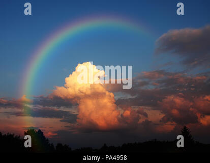 Una fotografia di una nuvola bianca in serata sole sotto un arcobaleno Foto Stock