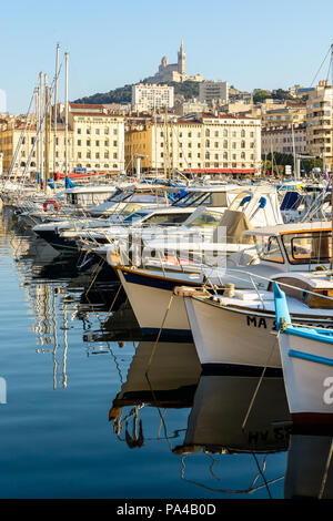 Il vecchio porto di Marsiglia, Francia, al tramonto con barche riflettendo in acque ferme e la basilica di Notre Dame de la Garde sulla sommità della collina. Foto Stock