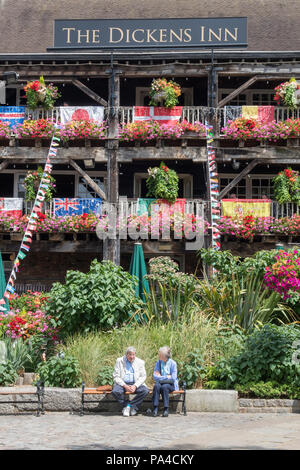 Una coppia di anziani al di fuori seduta di Dickens in public house a St Katherine docks nel centro di Londra. display floreali di public house di Londra Foto Stock