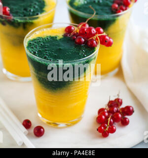 Due colori freschi frullati in bicchieri con frutti di bosco freschi. orange succo di banana con spirulina in polvere. detox prima colazione. Il mangiare sano Foto Stock