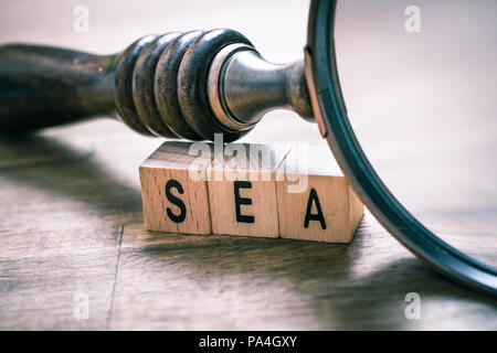 Vintage lente di ingrandimento appoggiandosi sui blocchi del mare su un vecchio tavolo di legno - Motore di ricerca il concetto di pubblicità Foto Stock