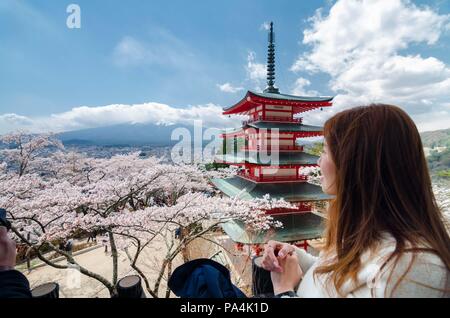 Ritratto di dolce e bella ragazza asiatica ammirando il maestoso Monte. Fuji presso la piattaforma di osservazione della Pagoda Chureito, circondato da fiori di ciliegio Foto Stock