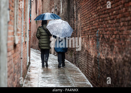 Le donne a piedi su uno stretto vicolo (street) e nascondere sotto ombrellone durante un giorno di pioggia a Venezia, Italia Foto Stock
