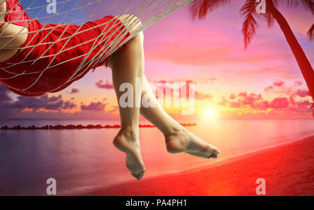 Close-up sulle gambe di una donna giaceva in una amaca e godersi il tramonto sulla spiaggia