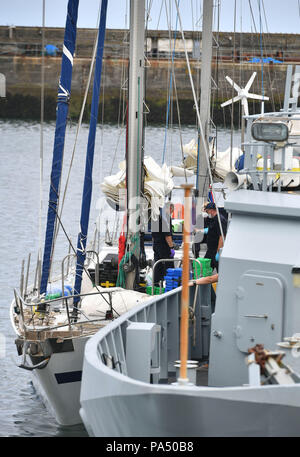 I farmaci vengono scaricati da una barca da ufficiali a Newlyn Harbour, con il bordo tagliente di forza HMC Vigili (a destra), dopo la criminalità nazionale agenzia grippaggio di uno yacht a vela nel Canale della Manica e comprato indietro verso il porto e arrestato due uomini per sospetto di traffico di stupefacenti. Foto Stock