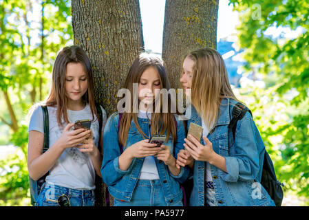 Le tre ragazze fidanzate studente. In estate nel parco dalla struttura ad albero . Nelle mani di trattenere gli smartphone. È corrispondeva in reti sociali. Concep Foto Stock