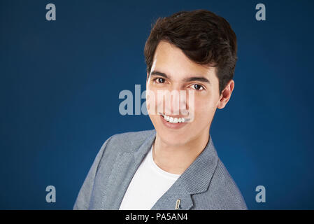 Ritratto di giovane uomo sorridente con i capelli scuri isolati su sfondo blu Foto Stock