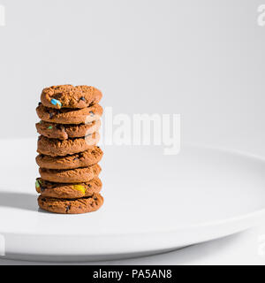 Choc chip smarties cookies impilati su una piastra bianca. Foto Stock