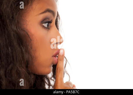 Profilo di una giovane e bella di carnagione scura la donna con il dito sulle labbra su uno sfondo bianco. Concetto di silenzio Foto Stock