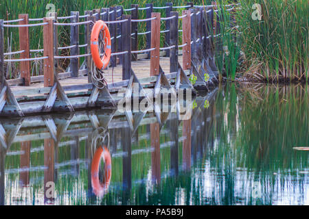 Close up di serena Passerella galleggiante con orange salvagente riflessa nell'acqua Foto Stock