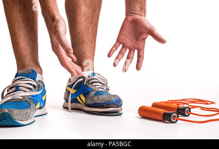 Uomo che guarda verso il basso nel senso di frustrazione a sua usurata coppia di scarpe da ginnastica. Foto Stock