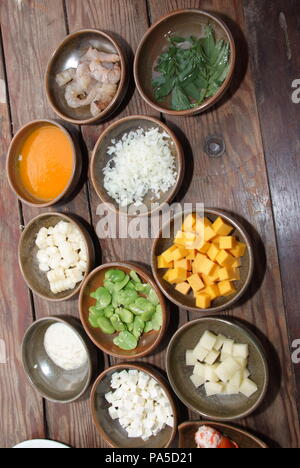 La cucina peruviana, 'Chupe de camarones': un srwimp zuppa di latte, cipolle, e spogliatoio con fine erbe chiamato 'huacatay'. Gli ingredienti su un tavolo di legno. Foto Stock