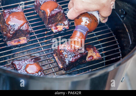La cottura di una marinata di costolette di manzo su un barbecue esterno e irrorare con la salsa Foto Stock