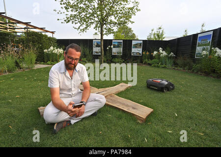 Würzburg, Germania. 04 Luglio, 2018. Alexander Seufert controllare un robot lawnmowing con il suo smartphone in "time-salvataggio Garden' in Baviera Garden Show. Il giardino progettato da questo master giardinaggio mostra che il giardino digitale non è una cosa di più il futuro. Credito: Karl-Josef Hildenbrand/dpa/Alamy Live News Foto Stock
