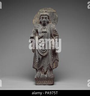 Bodisattva permanente (Maitreya Buddha del futuro). Cultura: Pakistan (antica regione del Gandhara). Dimensioni: H. 31 3/4 in. (80,7 cm); W. 11 1/2 in. (29,2 cm); D. 6. (15,2 cm). Data: ca. 3. secolo. Maitreya è il Buddha della prossima età, per quanto è di Shakyamuni Buddha della nostra epoca. Egli risiede in Paradiso Tushita aspettando il suo finale di rinascita. Come si addice il suo più alto rinascita, indossa i capi di abbigliamento e gioielli di un principe, sebbene la sua aureola demarks chiaramente il suo stato divinizzato. Egli può essere identificato dall'acqua sacra pallone nella sua mano sinistra. Museo: Metropolitan Museum of Art di New York, Stati Uniti d'America. Foto Stock