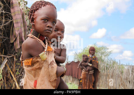 Una ragazza Hamer porta il suo fratello durante il Bull Jumping cerimonia (Ukuli rituale) da Hamer Hamar tribù, Etiopia Foto Stock