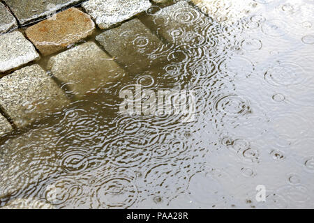 Pioggia in città - pozzanghere sulla strada di ciottoli pavimentazione - acqua gocce di pioggia Foto Stock