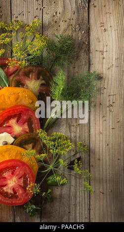 Pomodori maturi, aneto, foglie di basilico e una fetta di formaggio giacciono su schede di colore grigio. Intorno i semi di aneto sparse Foto Stock